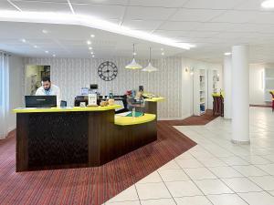 a man standing at a counter in an office at Terres de France - Appart Hôtel Rouen Flaubert in Rouen