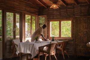 a woman setting tables in a room with windows at Souimanga Lodge in Fimela