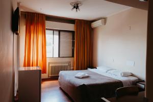 a bedroom with a bed and a window with orange curtains at Hotel Letto Caxias in Caxias do Sul