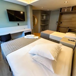 a room with three beds and a tv on the wall at Hotel Zata e Flats in Criciúma
