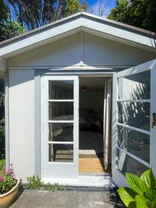 a small white shed with a door open at Ruby Bay Beach Sleepout - 30 mins from Abel Tasman in Mapua +8 photos