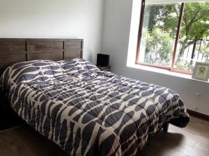 a bed with a black and white comforter and a window at Casa del Parque in Talca