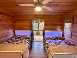 two beds in a log cabin with a ceiling fan at Riverfront Blue Jay Cabin in Murphy