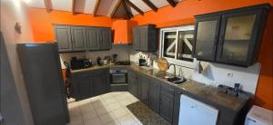 a kitchen with black cabinets and an orange wall at Au cœur de douenel bouillante cheques vacances acceptées in Bouillante