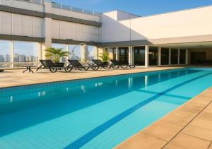 a swimming pool with chairs and a building at Hotel Guarulhos Flat 2004 in Guarulhos