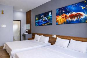 two beds in a hotel room with paintings on the wall at Hoa Dã Qùy Hotel 2 in Pleiku