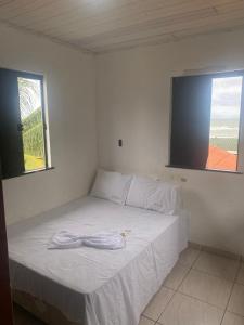a bedroom with a white bed with two windows at Cabana Maktub in Uruçuca