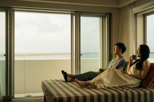 a man and woman sitting on a bed in front of a window at THE SENAGAJIMA STORYLINE in Tomigusuku
