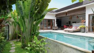 a pool with a palm tree next to a house at Karma House Ungasan in Jimbaran