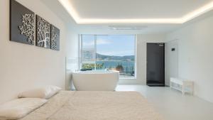 a white bedroom with a bath tub and a large window at Geoje Badageurigo Pension in Geoje