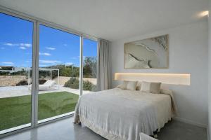 a white bedroom with a bed and a large window at Villa Codolar in Cala Morell +13 photos