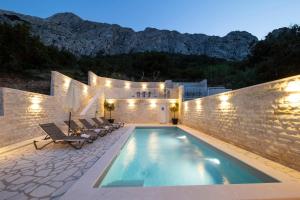 a swimming pool with chairs and a building with mountains at VILLA PAG - SVETA MARIJA in Pag