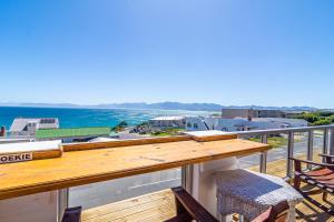 a balcony with a wooden table and chairs and the ocean at Whale Heights in De Kelders