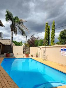 a blue swimming pool with a fence and a palm tree at Tuscany Vryburg in Vryburg