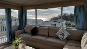 a living room with a couch and a large window at Driftwood at Freshwater Beach Holiday Park in Burton Bradstock