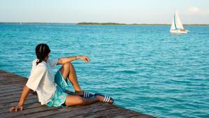 a woman sitting on a dock with a sailboat in the water at Hotel Diosa del Agua Bacalar in Bacalar