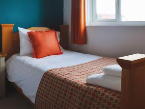 a bedroom with a bed with an orange pillow and a window at Headlands Hideaway in Coverack