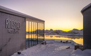 a building in the snow with a sunset in the background at Ringstad Resort in Bø