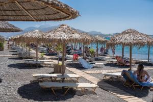a beach with many chairs and straw umbrellas at Estia Luxury Apartment in Ierapetra