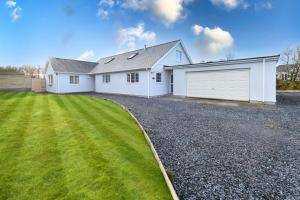 a white house with a driveway and grass at 5 Bed in Bryncroes oc-llecyn in Pwllheli