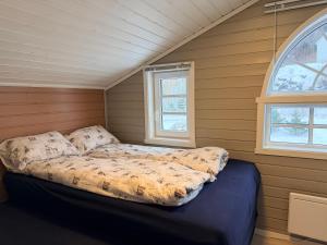 a bed in a small room with two windows at Sørlandets paradis in Svenevik