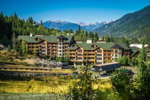 a large resort building with mountains in the background at First Tracks Lodge, by Lodging Ovations in Whistler