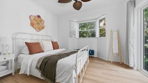 a white bedroom with a bed and two windows at Forries Beach Cottage in Wamberal