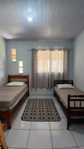 a bedroom with two beds and a window with a rug at Casa Rústica no centro de Araruama in Araruama