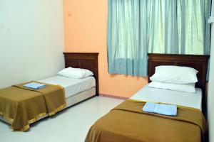 2 camas en una habitación con paredes de color naranja y cortinas azules en Homestay Kota Bharu, Telipot en Kota Bharu