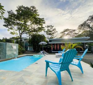 a swimming pool with two blue chairs and a house at La Jungla in Talamanca