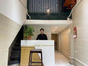 a man standing behind a counter in a hallway with a stool at Omeli homestay in Hanoi