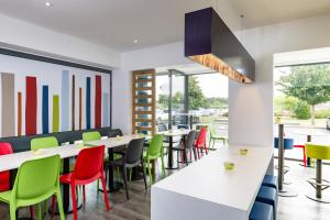 a dining room with white tables and colorful chairs at Ibis Budget Angers Parc des Expositions in Saint-Sylvain-dʼAnjou