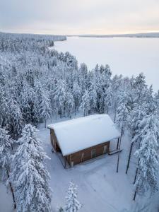 a cabin with snow on the roof in a forest at Lakeside Cabin in Romakkaniemi