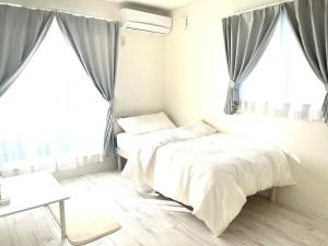 a white bedroom with two beds and windows at Sunny Inn Sumida in Tokyo