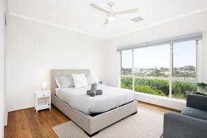 a white bedroom with a bed and a window at Beach by the Dunes in Goolwa South