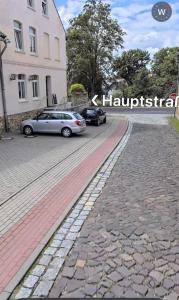 two cars parked on a cobblestone street next to a building at Tanne Grand Palace in Alleringersleben