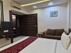 a bedroom with a bed and a chair and a television at Hotel Radiant Kolhapur in Kolhapur