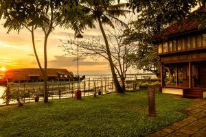 a house and a boat on the water with a sunset at Coconut Lagoon Kumarakom - A CGH Earth Experience in Kumarakom