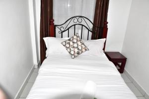 a bed with white sheets and a wooden headboard at Primestay Suites in Eldoret