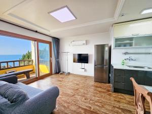a living room with a couch and a kitchen with a view at Tteuribada Pension in Seogwipo