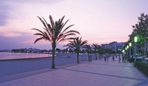 a sidewalk with palm trees and a beach at night at Hollywood Palazzo in Roses