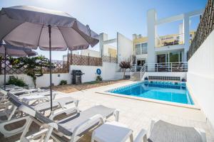 a pool with chairs and an umbrella next to a house at Villa Granada in Almancil