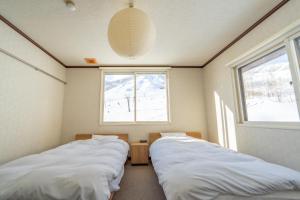 two beds in a room with two windows at 北国ロッヂ in Otari