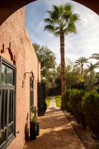 a palm tree next to a building with a sidewalk at Bab Akoul Palmeraie - Boutique Hotel & Spa in Marrakesh
