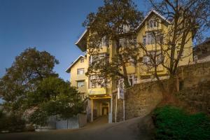 a yellow building on the side of a stone wall at Tripli Hotels Le Royale, Shimla in Shimla