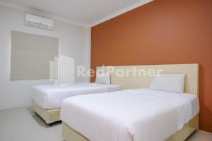 two beds in a room with white and orange walls at Hotel Andono near YIA Mitra RedDoorz in Yogyakarta