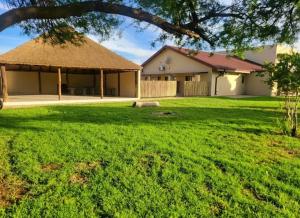 a large yard with a building with a grass roof at Indawo Guesthouse in Bloemfontein