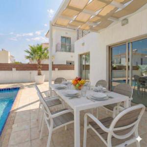 a white table and chairs on a patio with a pool at Fig Tree Beach Villa One in Protaras