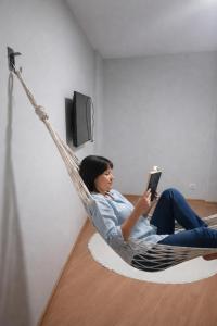 a woman sitting in a hammock reading a book at Apartamento Inteiro em Setor Nobre in Goiânia