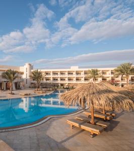 a resort with a swimming pool with a straw umbrella and benches at Hurghada Long Beach Resort in Hurghada